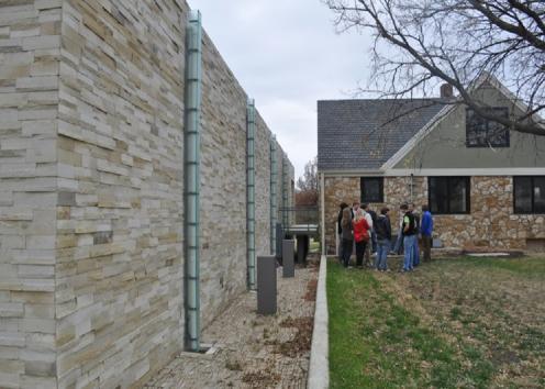 People gathering outside of a house next to a wall by the water treatment plant